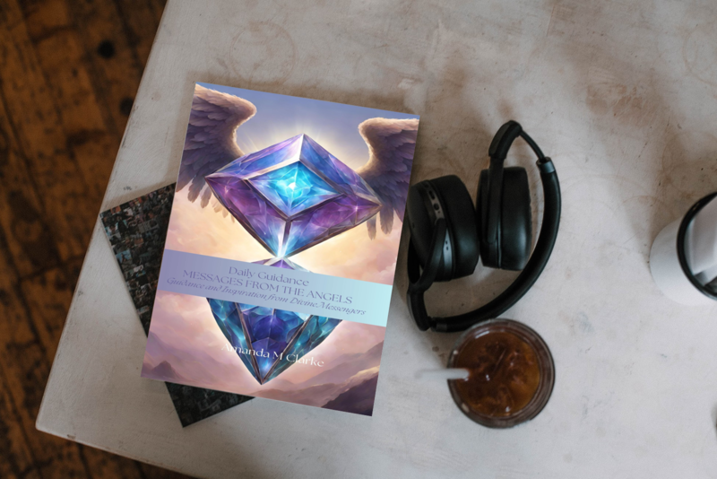 Book titled 'Messages from the Angels' with a pair of headphones and a mug on a marble surface.